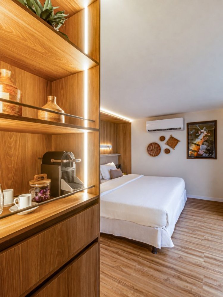 Detalhe da suíte com estante em madeira e cama ao fundo